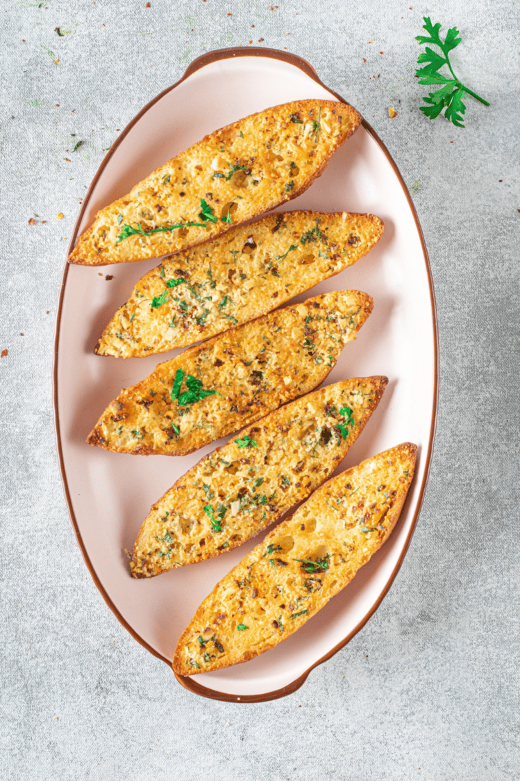 Close-up of air fryer garlic bread slices with toasted edges and visible herbs like parsley and basil.