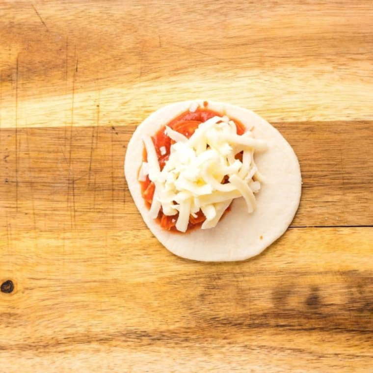 Filling dough squares with marinara sauce, cheese, and pepperoni.