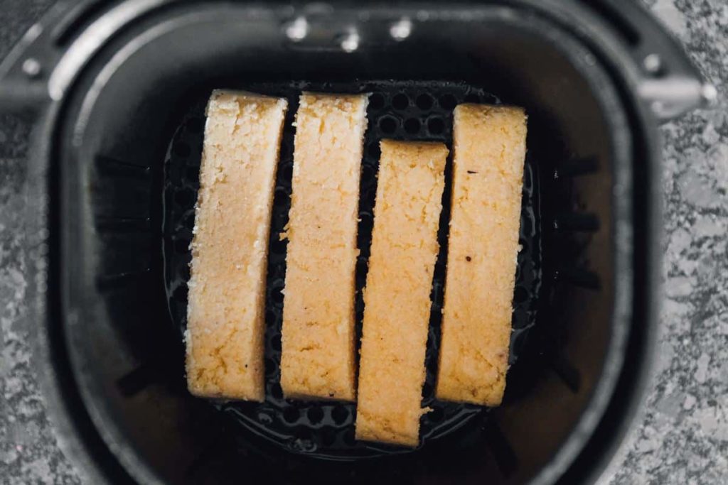 Firm polenta cut into thick fry-shaped sticks on a board