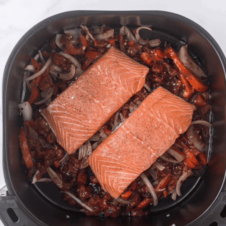 "Air fryer basket with seasoned salmon fillets and vegetables cooking at 400°F for 7-9 minutes."