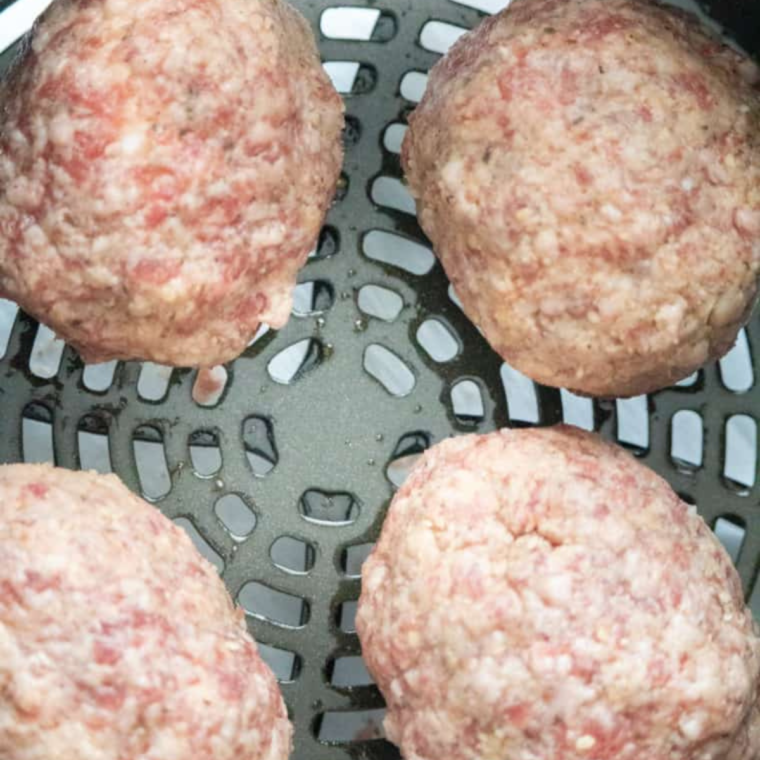 Scotch eggs arranged in air fryer basket cooking until sausage is golden and crispy
