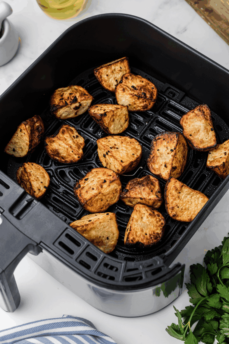 A bowl of crispy, golden-brown air fryer red potato wedges seasoned with herbs and garlic.