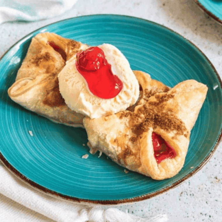 Flaky homemade cherry turnovers with icing drizzle on parchment paper