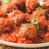 Olive Garden Meatballs served in marinara sauce, garnished with fresh herbs.