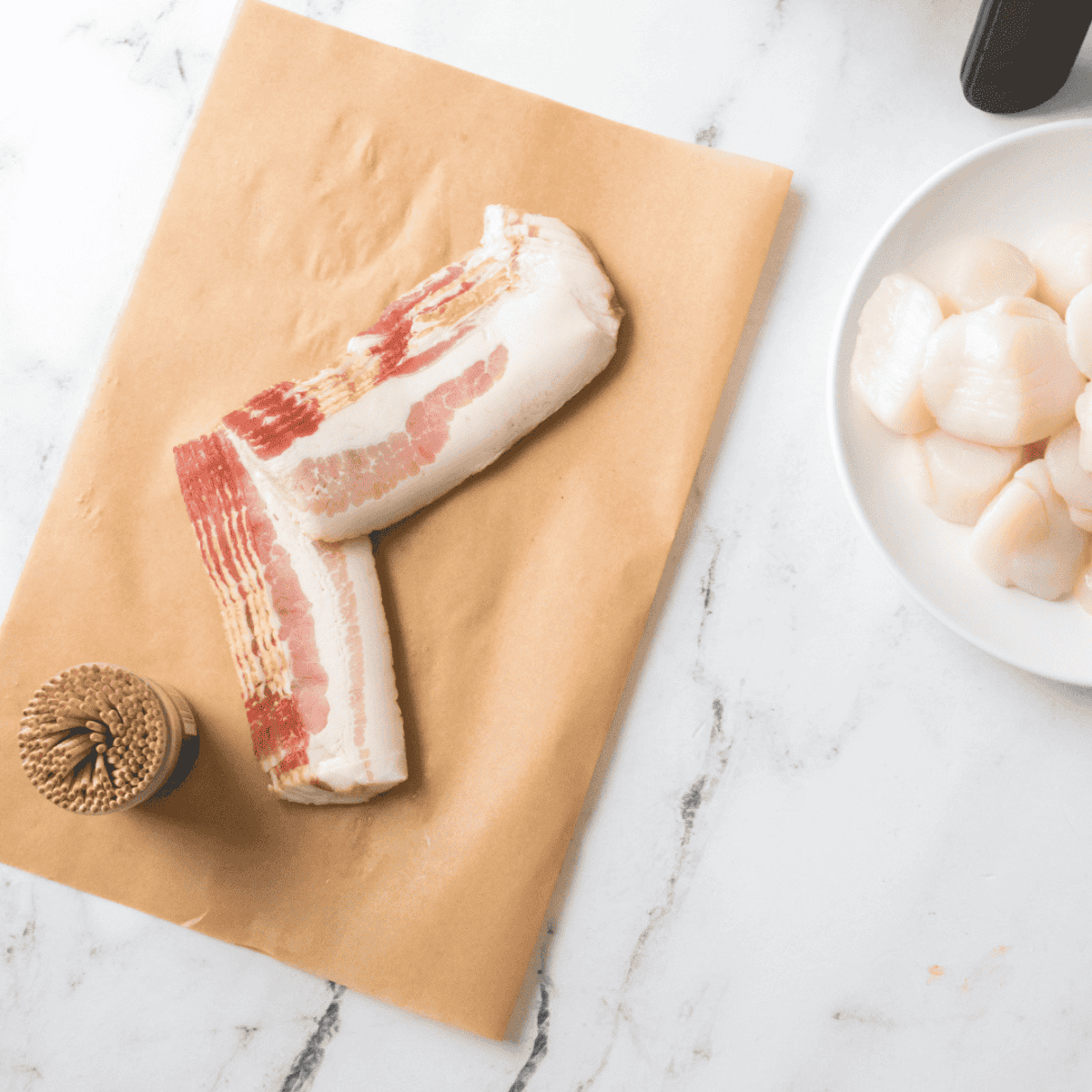 Wrapping scallops with bacon, using a toothpick to secure each piece.