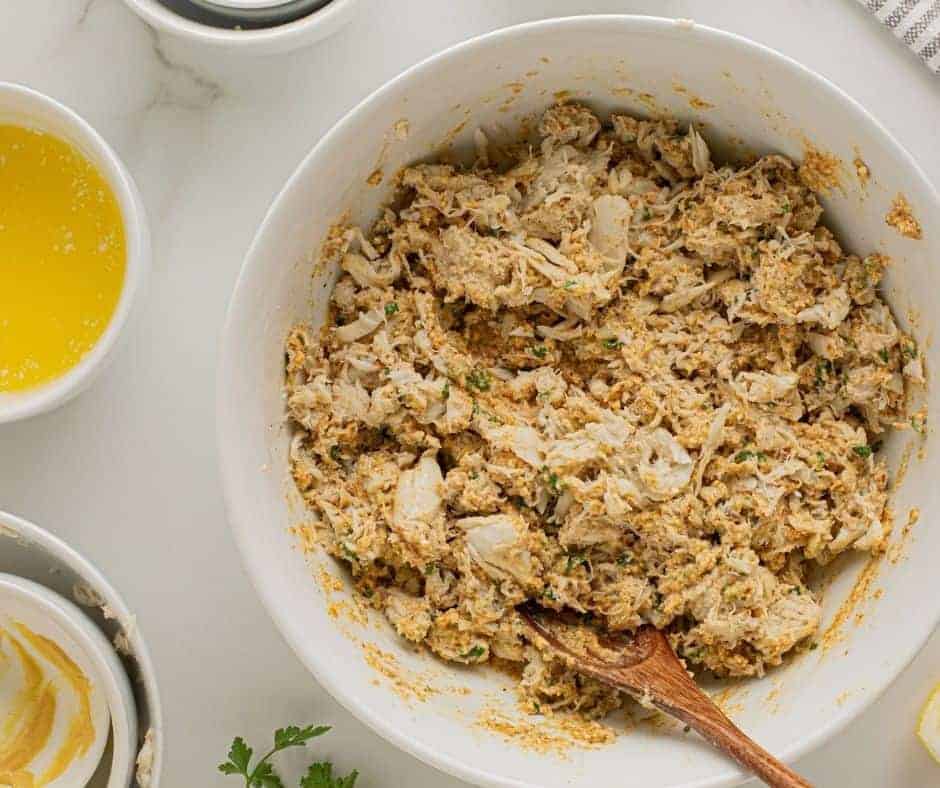 Mixing lump crab meat with seasonings and fillers in a large bowl.
