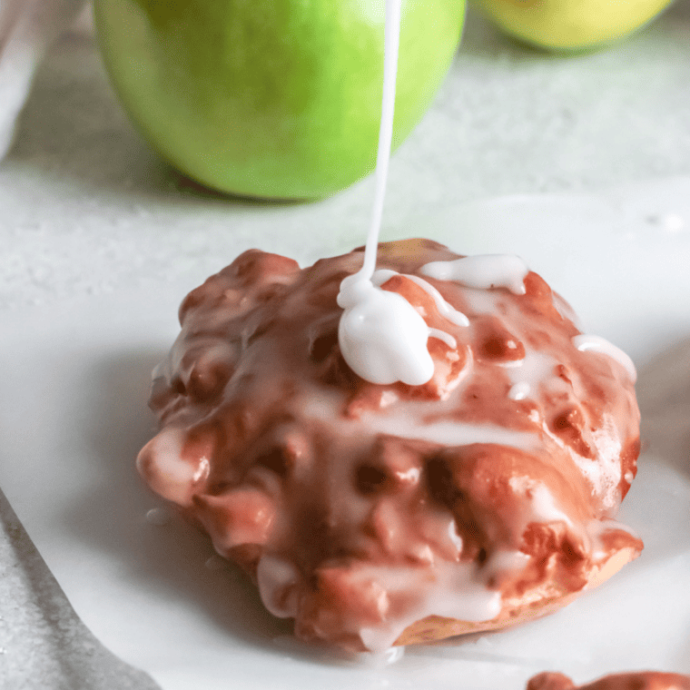Golden apple fritters on a wooden board with cinnamon and fresh apples
