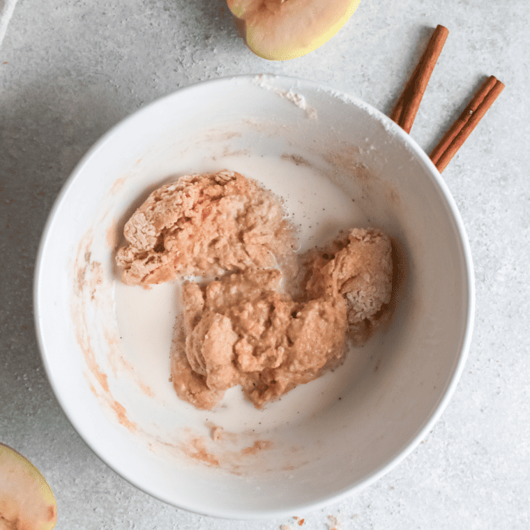 Apple fritter batter being stirred together in a glass mixing bowl