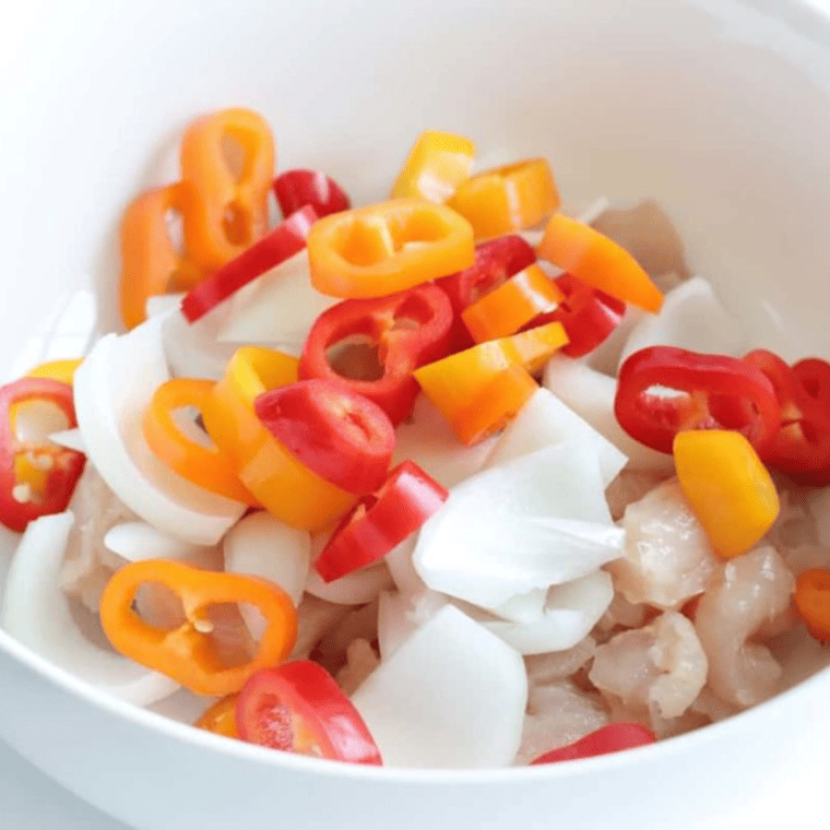 Chicken and pepper strips tossed with olive oil and fajita seasoning in a bowl
