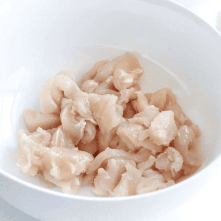 Raw chicken breast sliced into thin strips on a wooden cutting board