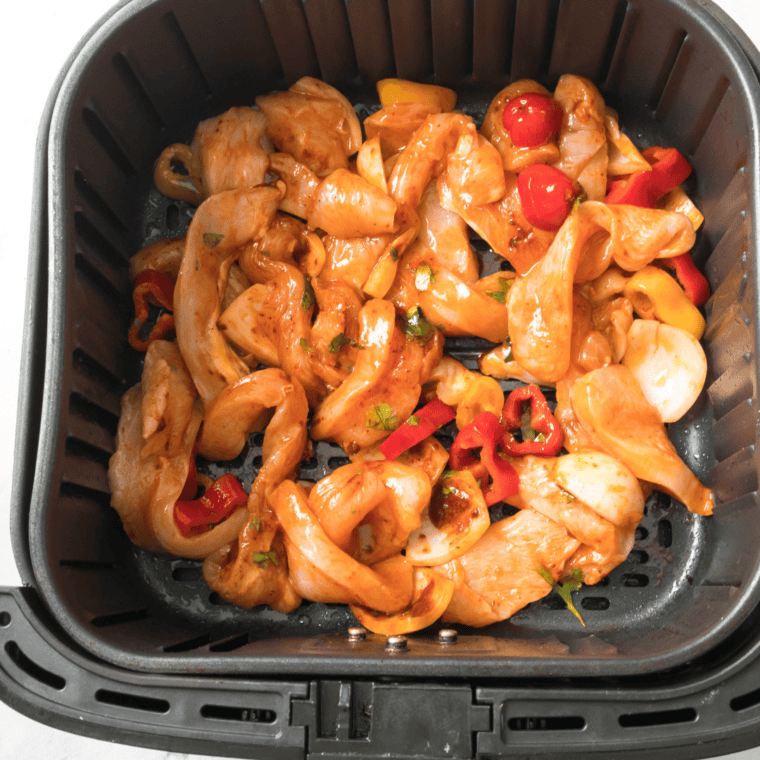 Seasoned chicken and peppers in a single layer in the air fryer basket