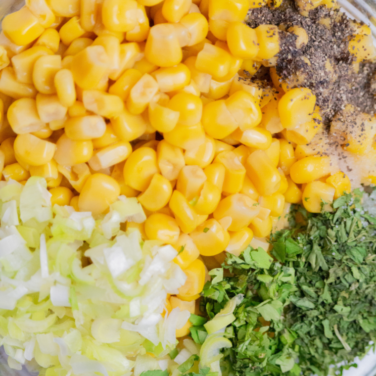Bowl filled with corn, scallions, cilantro, parsley, cheese, sour cream, and seasonings being mixed for chile relleno filling.