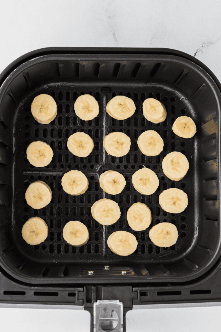 Slicing bananas into pieces and spraying air fryer tray with non-stick spray.
