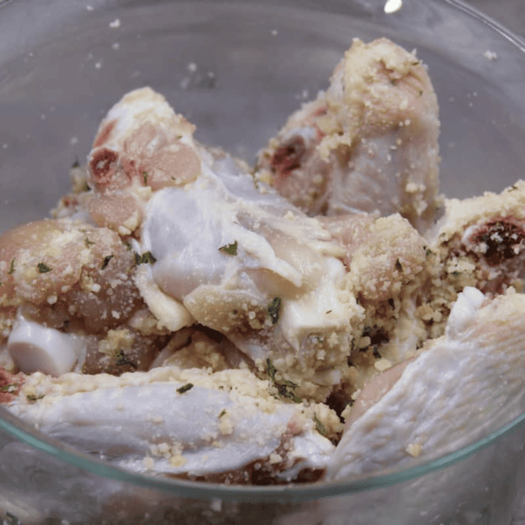 Chicken wings being tossed in a bowl with Parmesan cheese sauce, ensuring even coating.