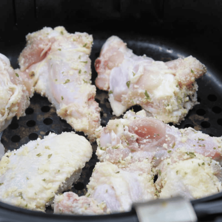 The air fryer with chicken wings is cooking inside, showing the delicious toppings.