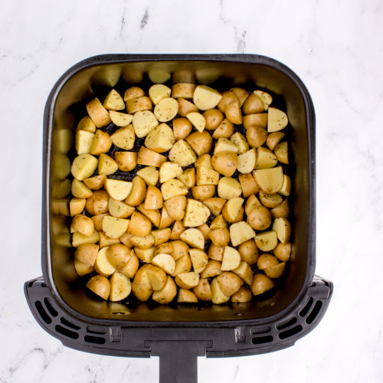 Seasoned potato pieces in a single layer in the air fryer basket