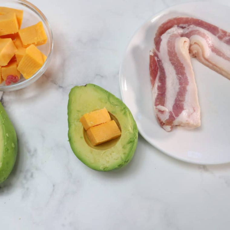 Halved avocados with pits removed, stuffed with diced cheddar cheese for burger bomb filling