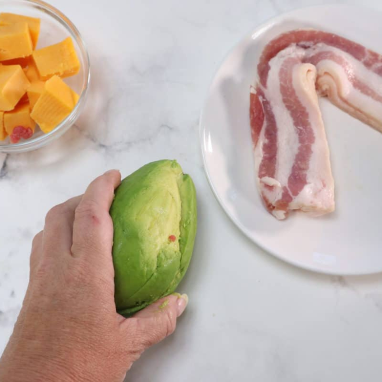 Placing the top half of the avocado back on to seal the stuffed avocado with cheddar cheese inside
