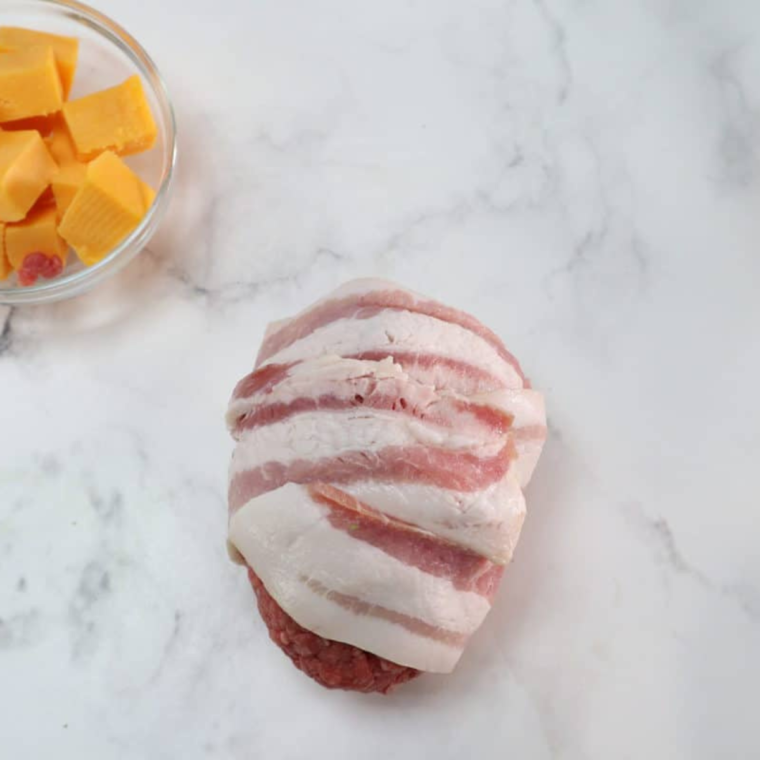 Wrapping bacon around the beef-covered avocado and placing it in the air fryer basket to cook at 350°F