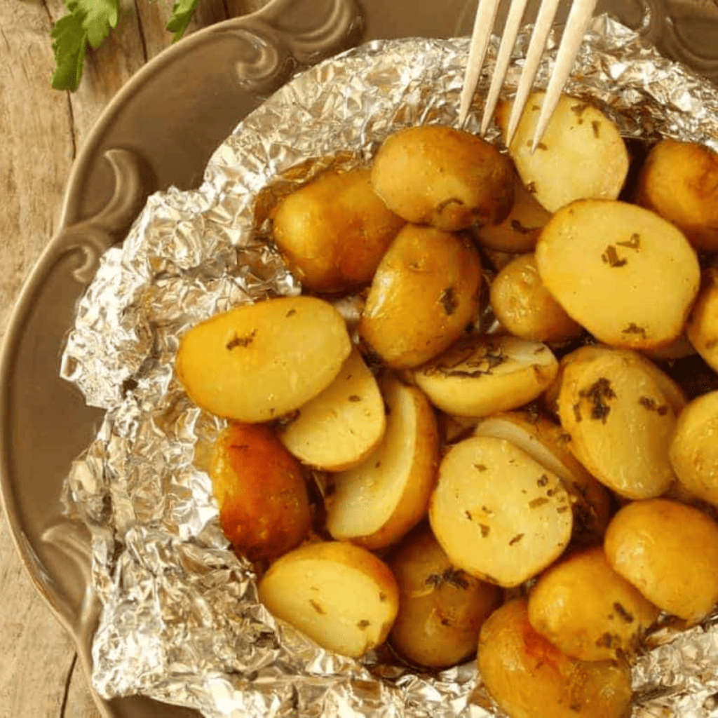 Plate of Air Fryer Foil Potatoes featuring crispy, golden-brown potato packs topped with melted cheese, crispy bacon bits, and fresh chives, served with a side of sour cream.