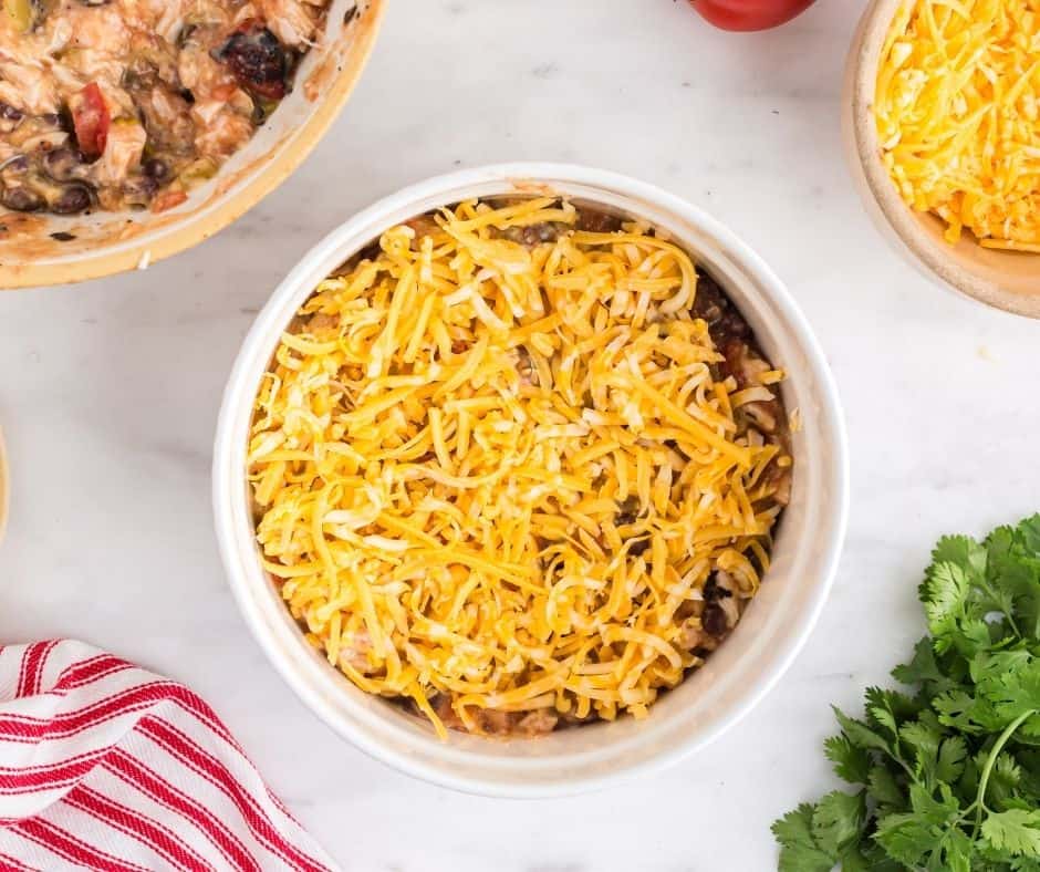 Sprinkling ground cumin over the chicken and bean mixture in a bowl.