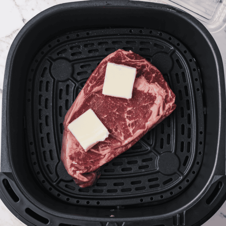 Two ribeye steaks seasoned with salt, pepper, and garlic powder ready for the air fryer.