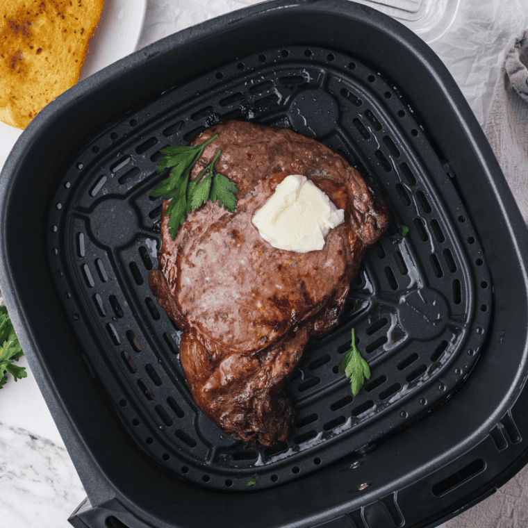Two ribeye steaks cooking in an air fryer basket at 400 degrees.