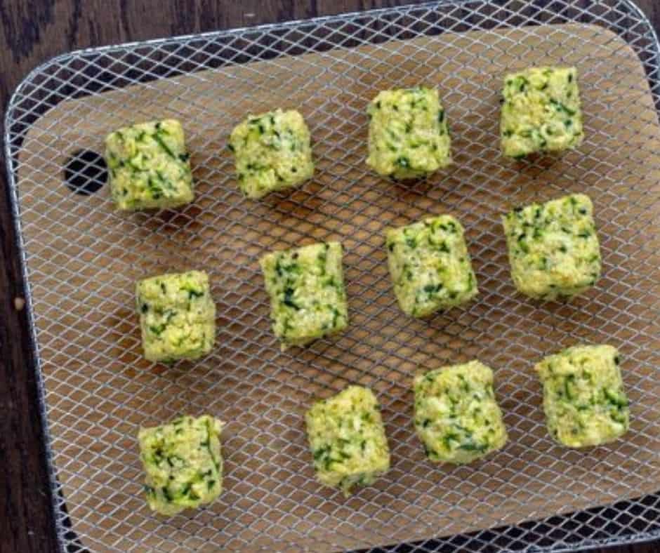 Shaping zucchini tots and placing them in an air fryer basket preheated to 350°F, cooking until golden brown and crispy.
