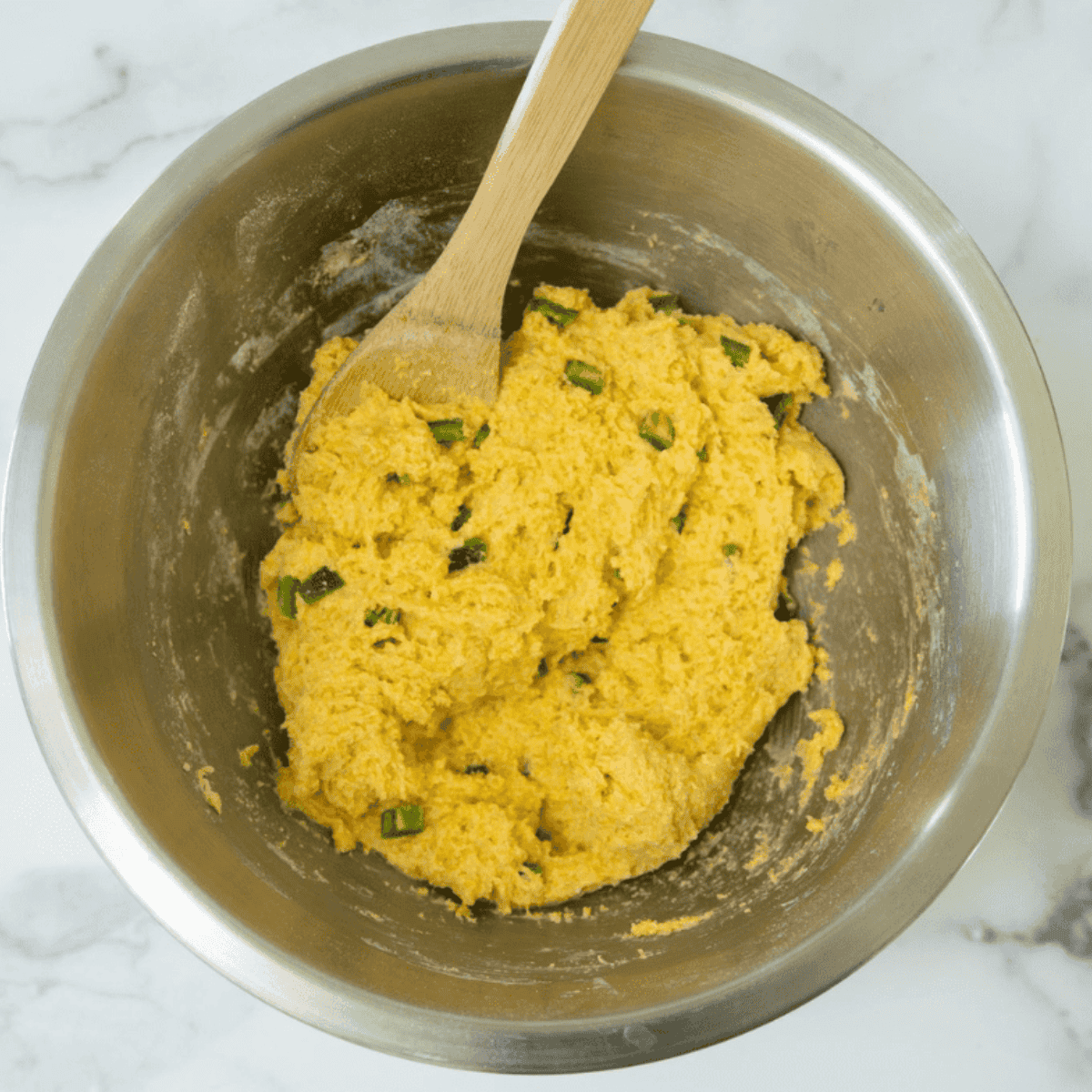 Adding flour, cornmeal, sugar, and baking soda to wet ingredients, then folding in diced jalapeños in a mixing bowl.