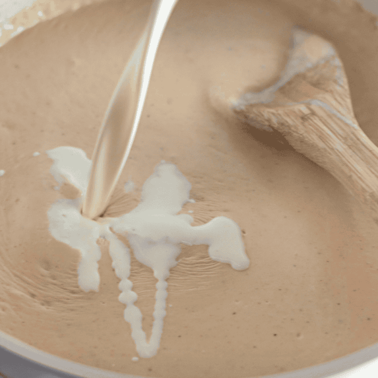 Pouring milk into flour mixture while whisking to thicken gravy, adding seasonings and adjusting taste