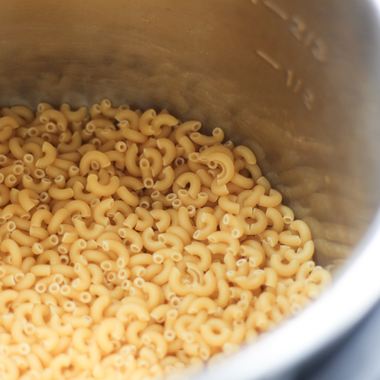 Dry elbow macaroni and water in an Instant Pot pressure cooker, ready to cook for the Panera mac and cheese copycat recipe