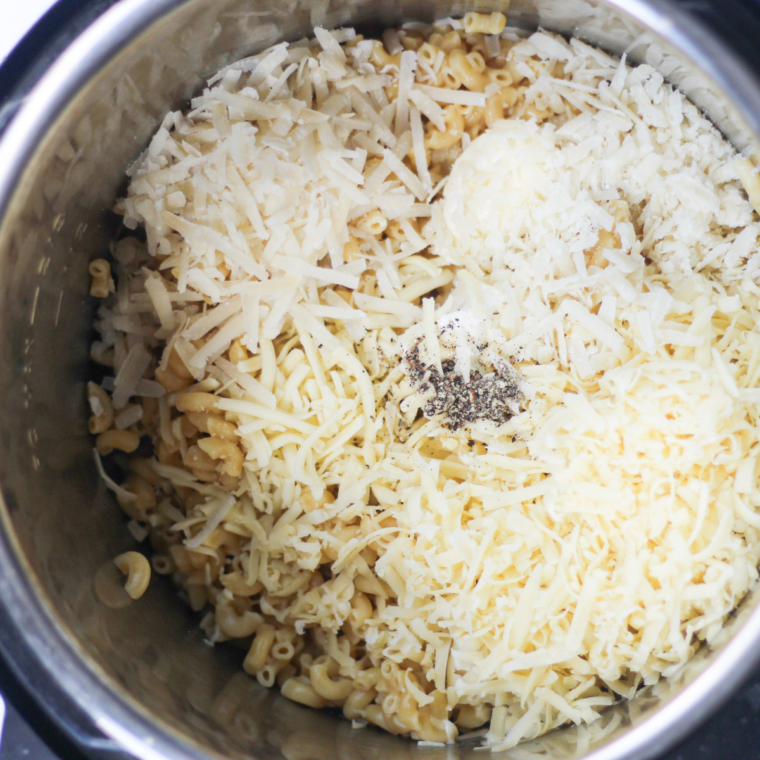 Shredded sharp white cheddar and torn American cheese slices being stirred into Instant Pot macaroni to make creamy Panera-style mac and cheese