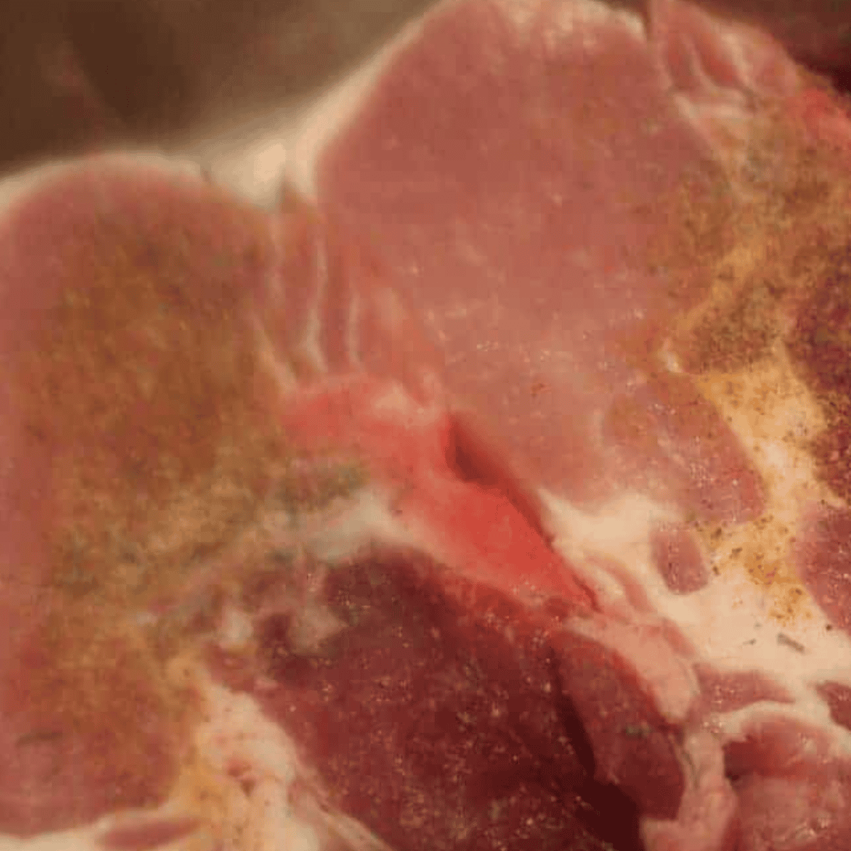 Seasoned pork chops being seared in olive oil on the pressure cooker.
