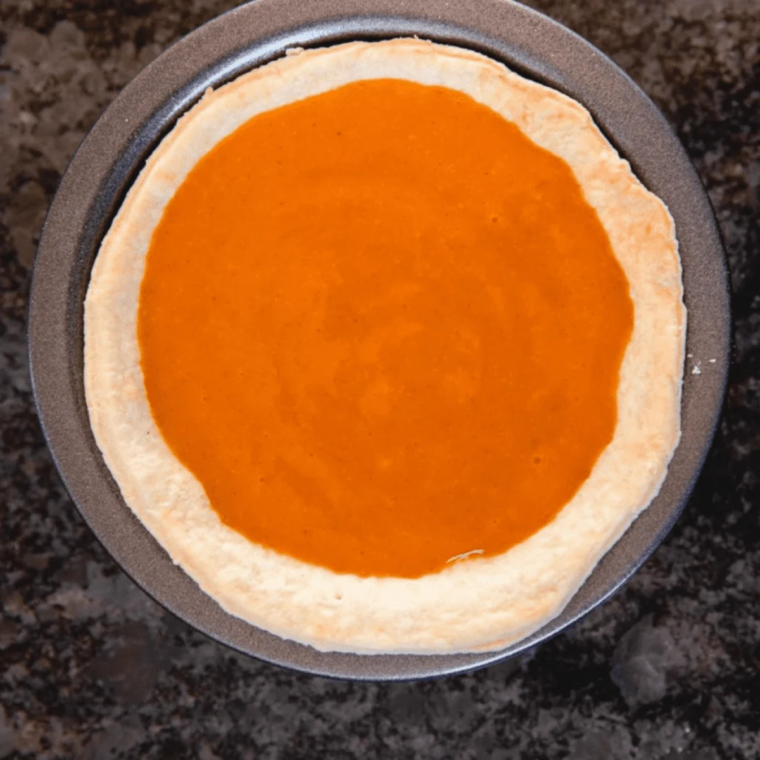 Pumpkin pie filling being poured into a chilled graham cracker crust in a springform pan
