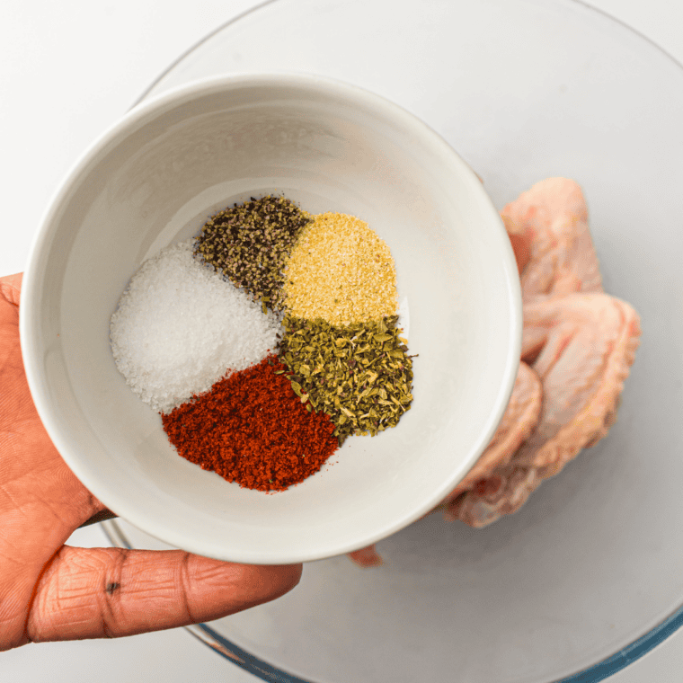 Tossing chicken wings with oil and seasonings in a mixing bowl