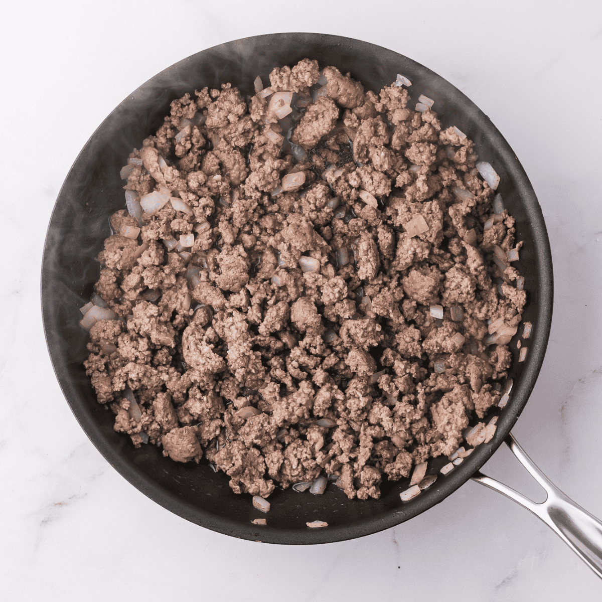 Ground beef and onions sautéing in a skillet with marinara sauce and seasonings.