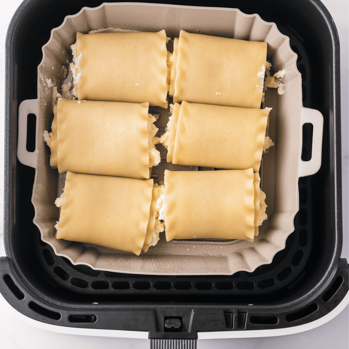 Lasagna rolls in an air fryer basket, covered with marinara sauce, ready to cook at 330°F for 10-12 minutes.