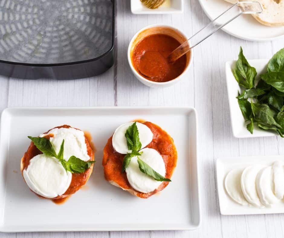 Bagels topped with mozzarella slices and fresh basil, ready for air frying.