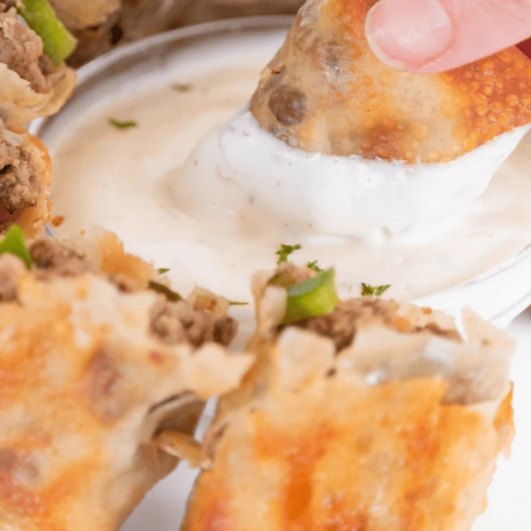 hilly cheesesteak egg rolls halved and standing upright on a platter with dipping sauce and parsley