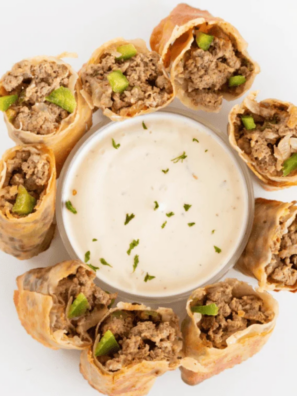 TGI Fridays Philly cheesesteak egg rolls sliced on the diagonal and stacked on a white plate with creamy horseradish dipping sauce