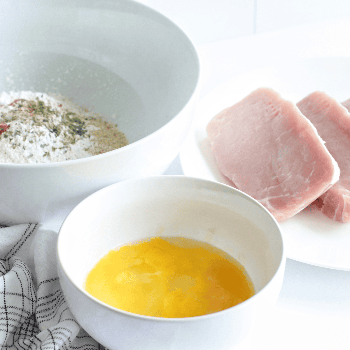 Seasoning pork chops and preparing flour, egg, and seasoning coatings.