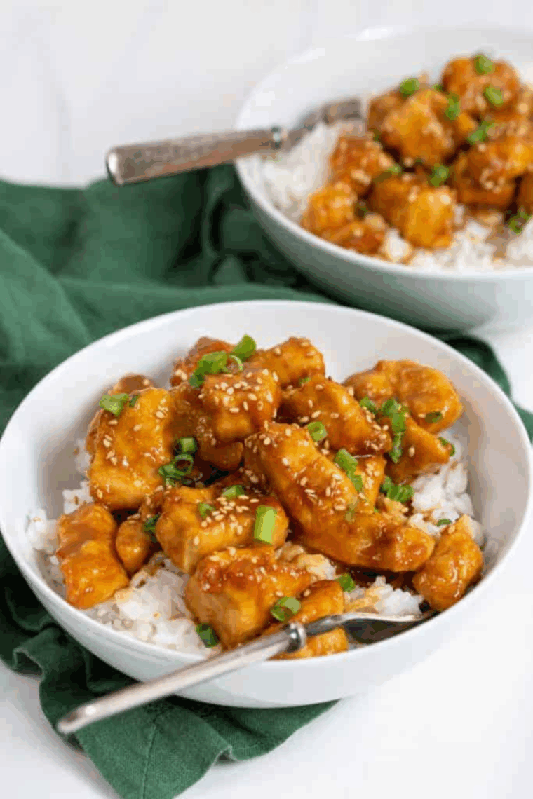 Crispy sesame chicken coated in glossy sauce, topped with sesame seeds and green onions.