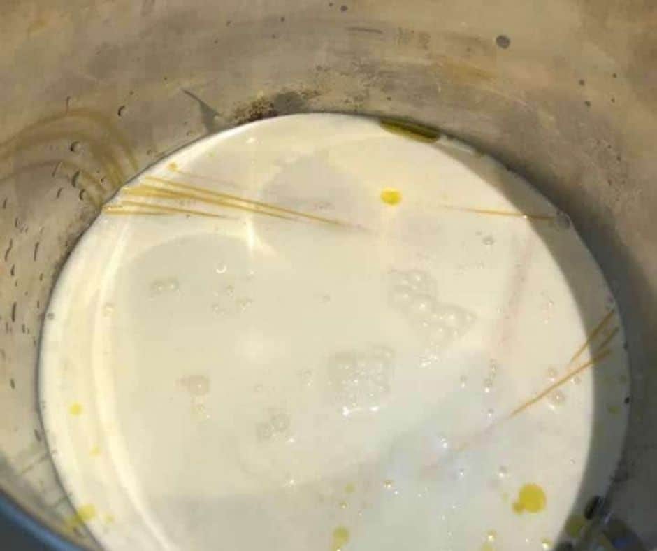 Pouring chicken broth over butter, olive oil, and minced garlic with broken pasta in the Instant Pot for copycat Parmesan Pasta Roni