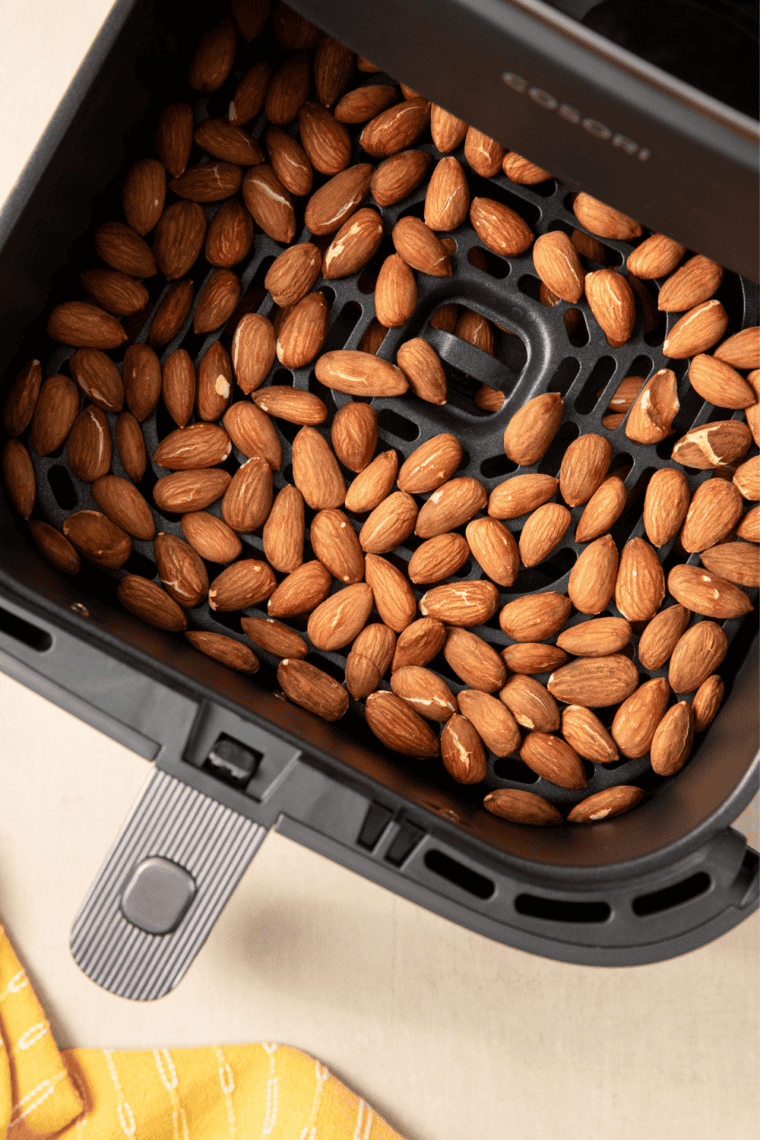 Raw almonds in a single layer in the air fryer basket before roasting