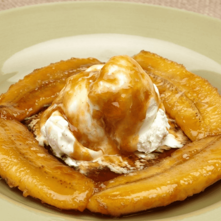 Close-up of caramelized bananas foster over French toast with whipped cream melting into the sauce