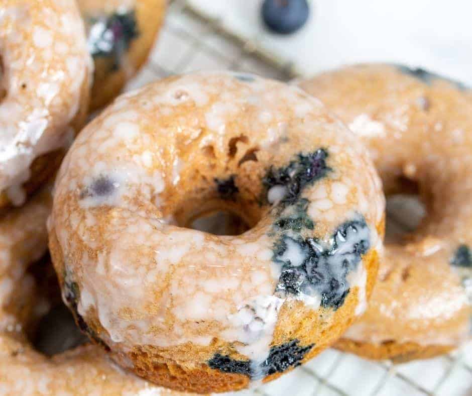 A plate of golden-brown blueberry donuts, freshly made in the air fryer, with a light glaze and a sprinkle of powdered sugar on top.