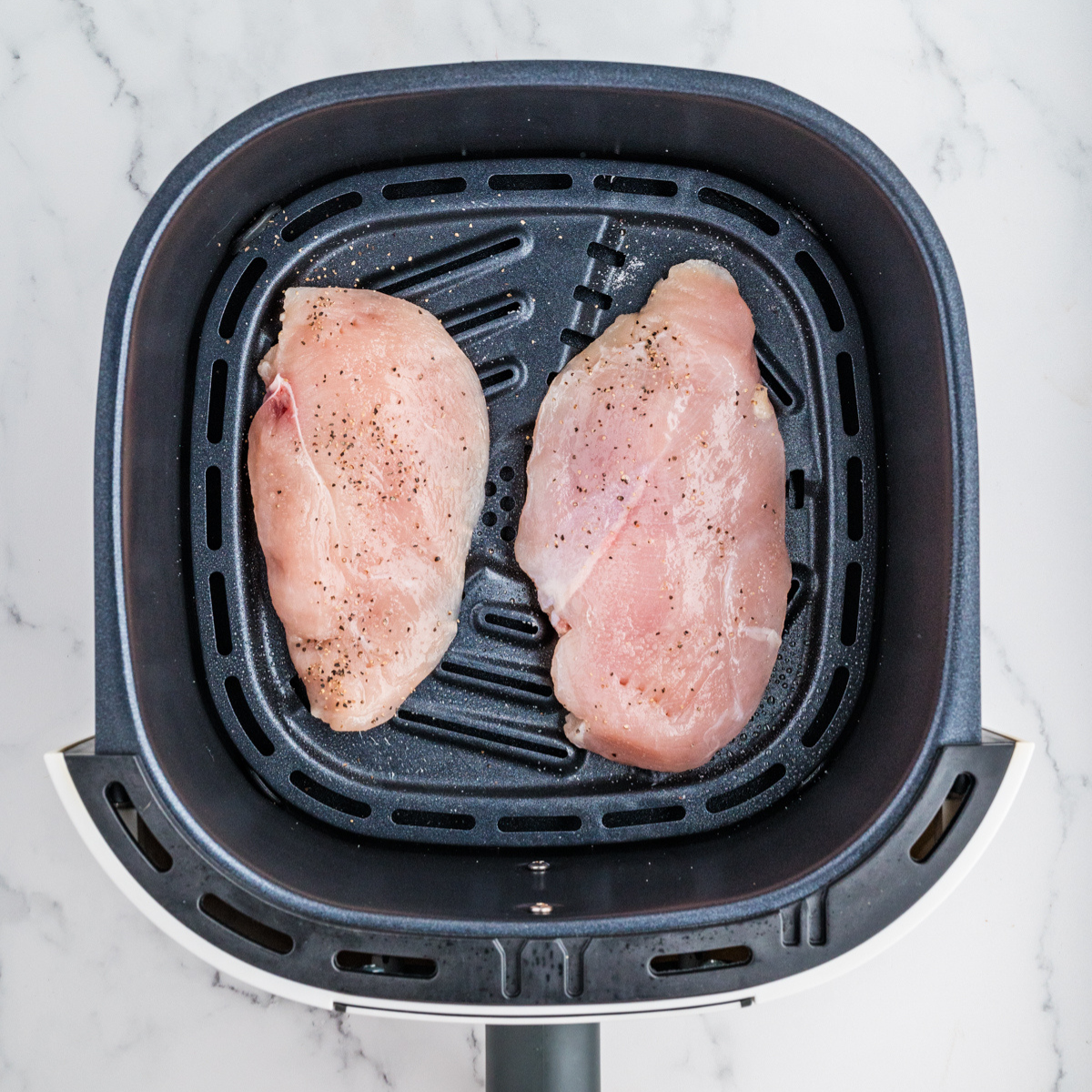 Close-up of seasoned chicken breasts and asparagus spears in the air fryer basket.