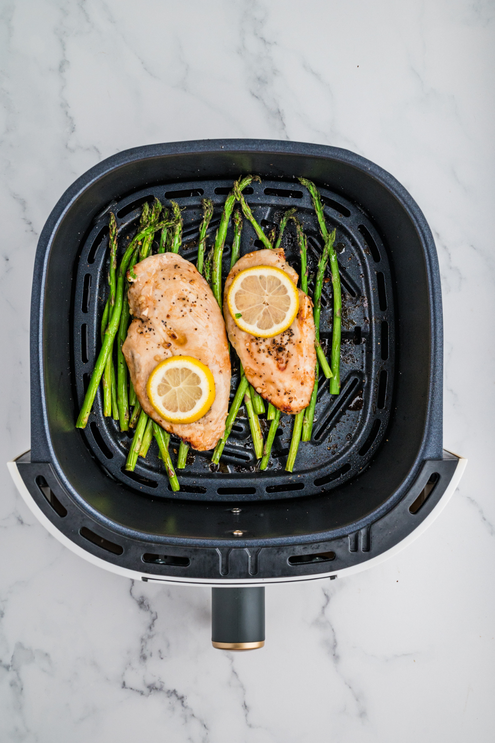 Close-up of seasoned chicken breasts and asparagus spears in the air fryer basket.