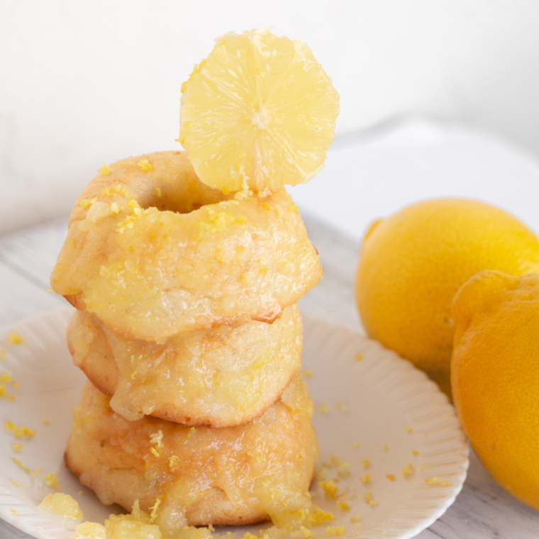 Fluffy air fryer lemon donuts covered in lemon glaze, stacked neatly on a white plate
