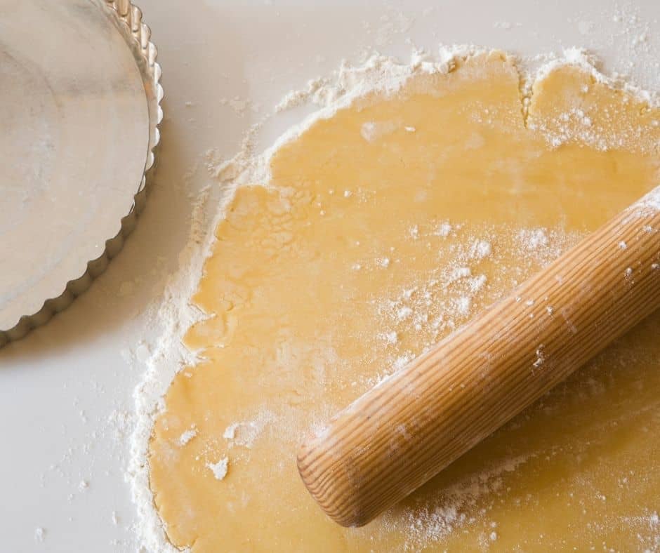 Rolling out pie dough on a floured surface, cutting a circle around a tart pan.